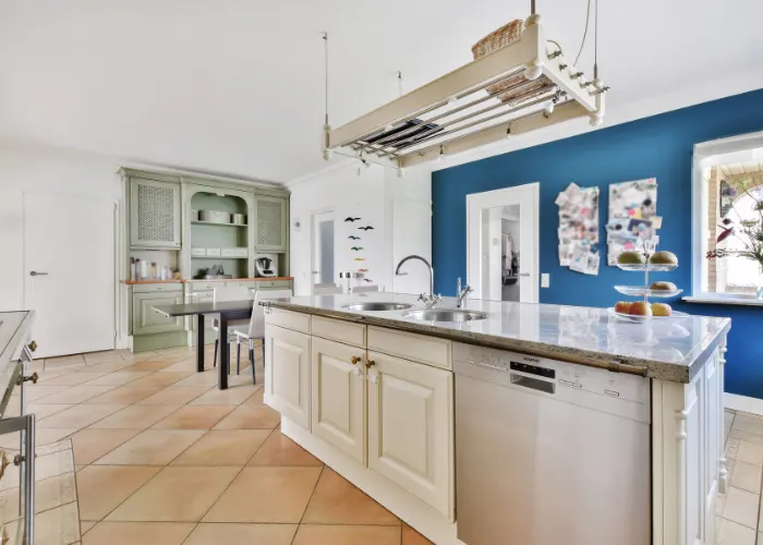 A big kitchen with blue walls a large center island with a hanging pot rack