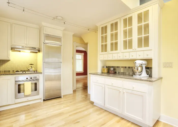 A newly remodeled kitchen with yellow walls, white lower cabinets & white  upper cabinets with glass insets